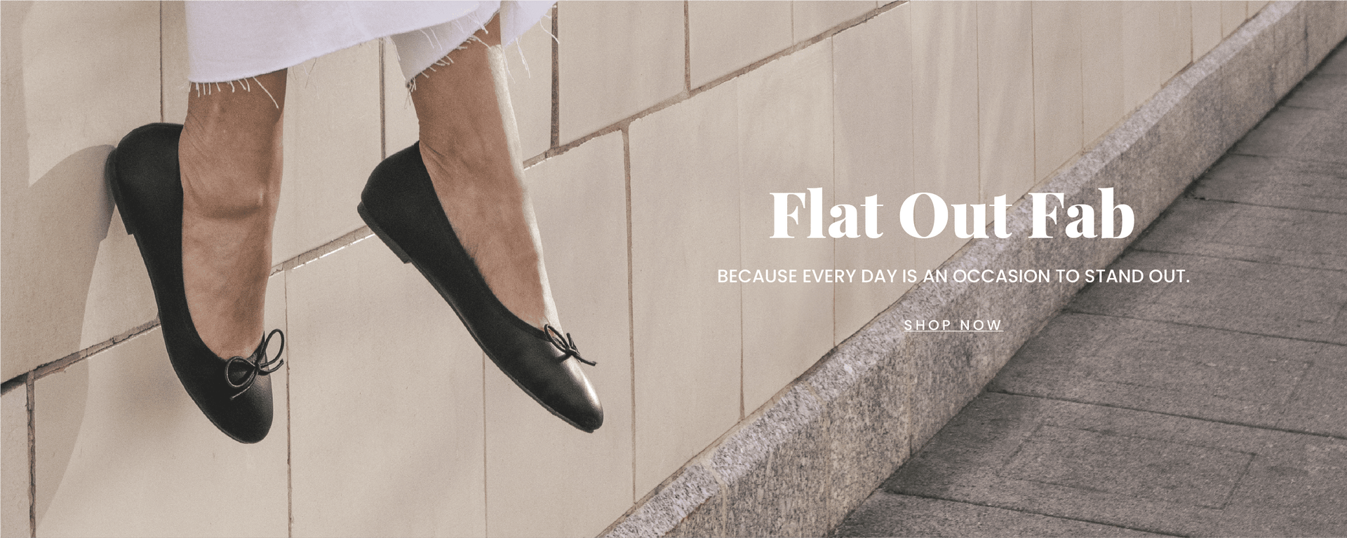 "Flat Out Fabulous" text in front of a background with a while building. A models legs are in view wearing a pair of classic black flats. "Shop Now" call to action links to the collection.