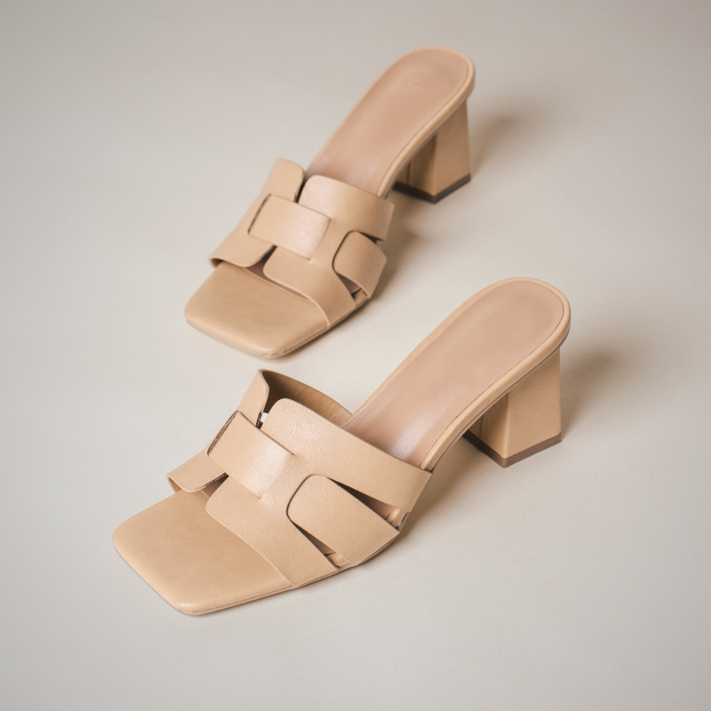 Pair of beige block-heeled slide sandals with wide interwoven straps, placed on a light background.