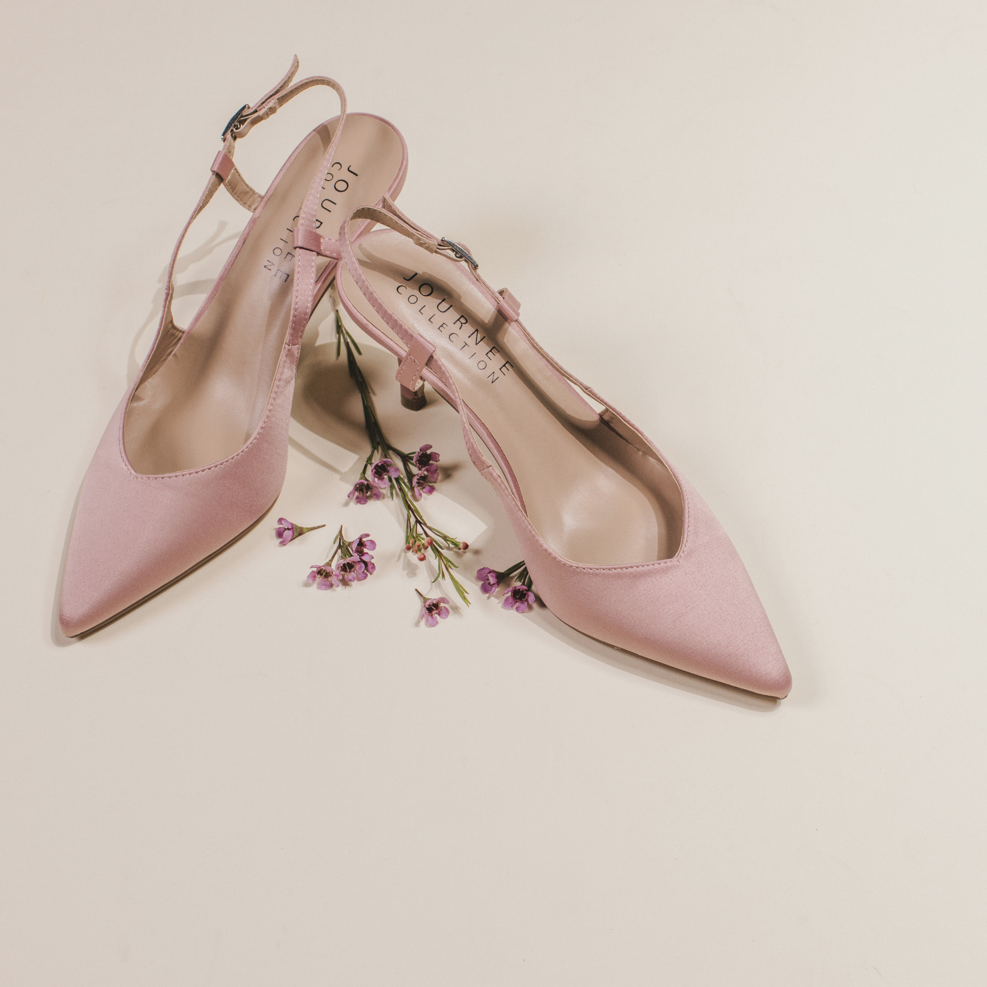 Pair of pink pointed-toe slingback heels styled with small purple flowers on a light background.