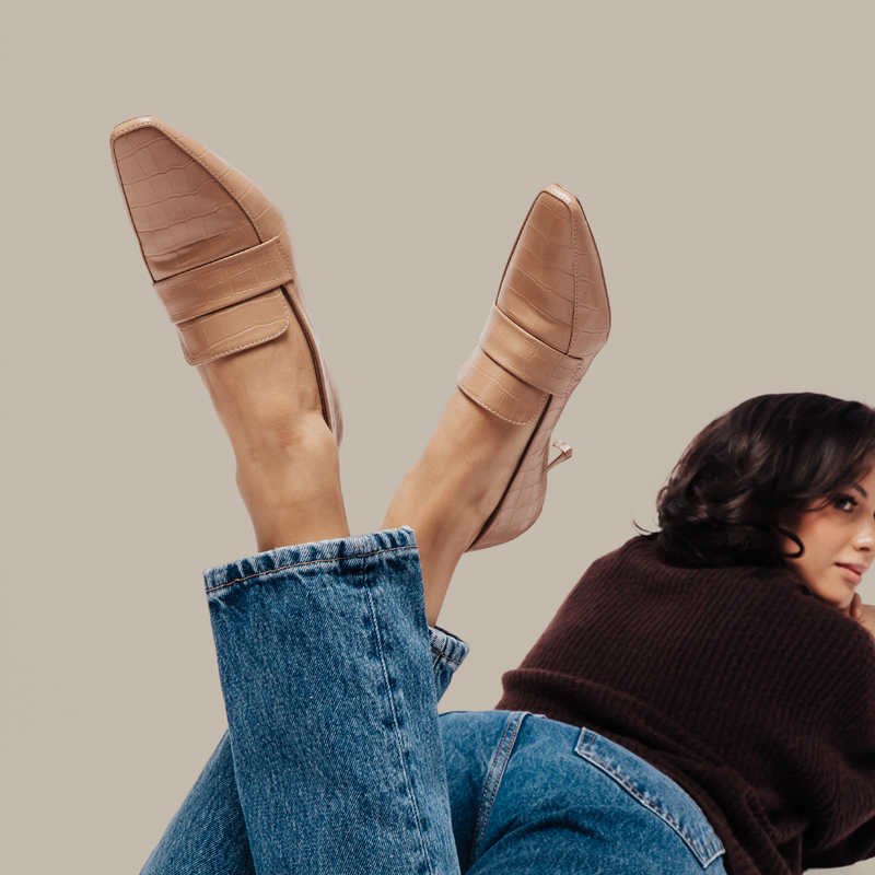 Close-up of a woman’s legs wearing tan pointed-toe kitten heels with a textured finish, paired with blue jeans.