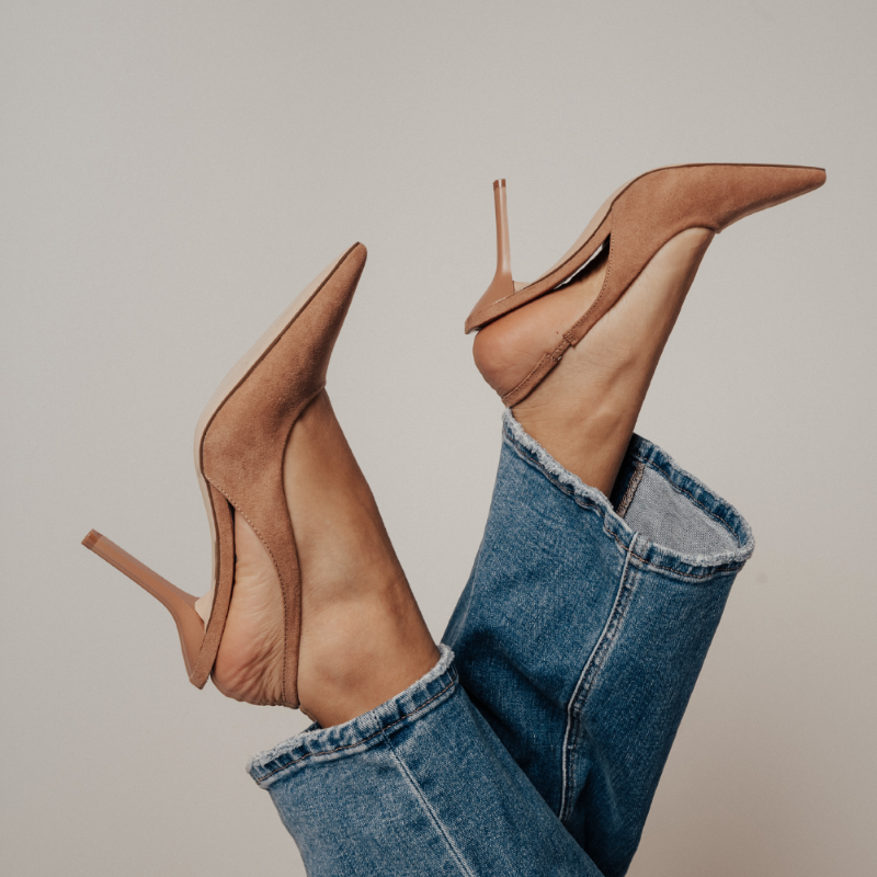 Close-up of tan suede pointed-toe slingback heels paired with cropped blue jeans, with legs playfully lifted in the air.