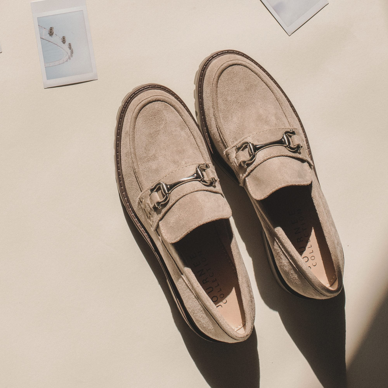 Pair of beige suede loafers with metal bit detail, styled against a light background with small photographs nearby.