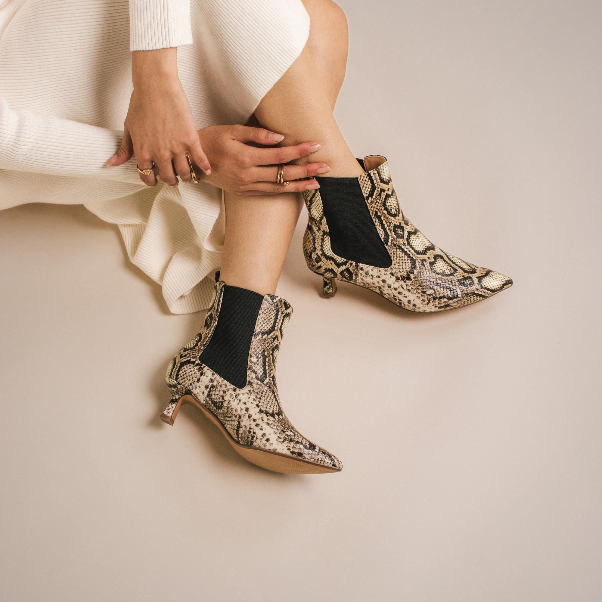 Close-up of a pair of pointed-toe ankle boots in a bold snakeskin print, styled with a white ribbed dress.