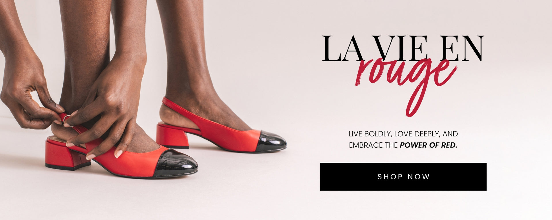 Close-up of a person adjusting the strap on red slingback heels with black patent leather toe caps and chunky heels, set against a minimalist off-white background. Text overlay reads 'La Vie En Rouge: Live boldly, love deeply, and embrace the power of red.' A black 'Shop Now' button is included.