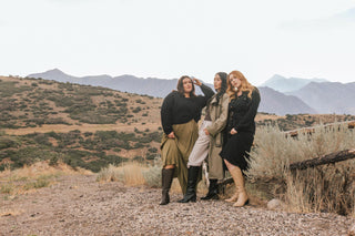 Three diverse women standing confidently in a scenic, mountainous landscape, showcasing a stylish range of knee-high boots in neutral tones. They wear fall-inspired outfits, blending fashion-forward designs with nature, embodying confidence and comfort. Header: "Fall for All" CTA button "Shop Now"