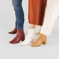 Three people wearing ankle boots in different colors: burgundy, cream, and tan, styled with jeans, a rust-colored skirt, and cream pants.