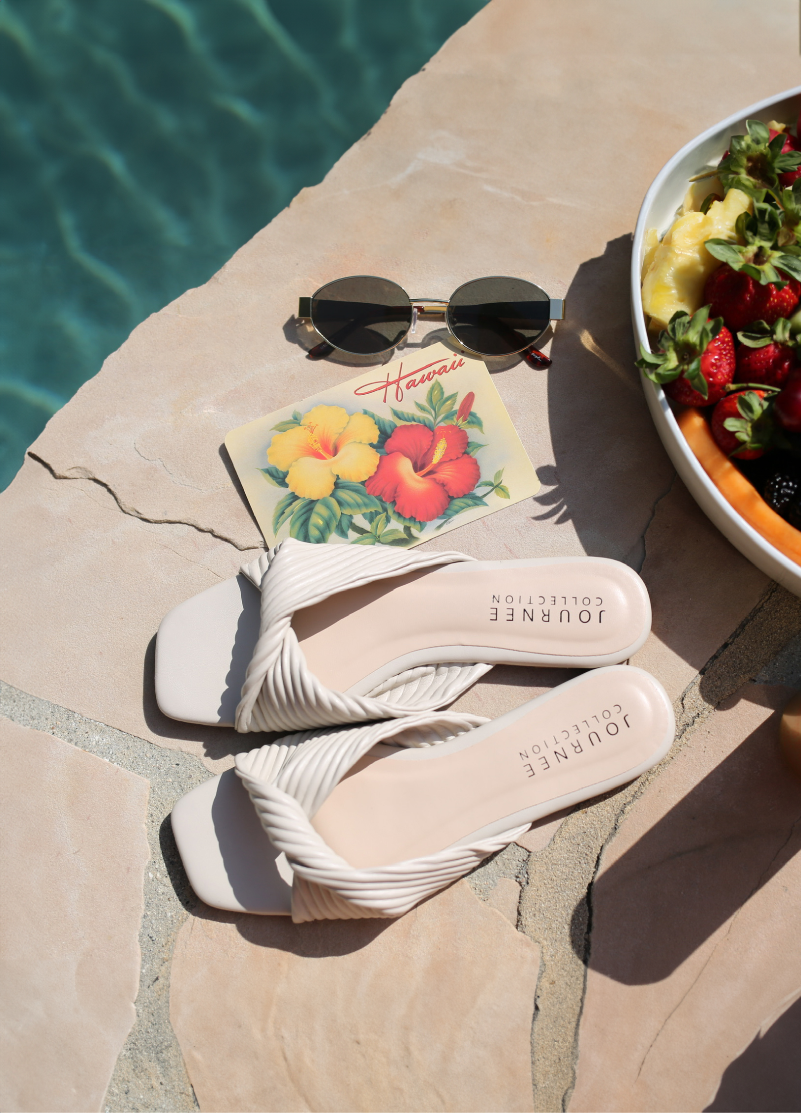 "Postcards from Paradise" header text with "find you perfect pair" subtext. Journee collection slide sandals in cream sit by a pool side next to a bowl of fruit, sunglasses, and post card. "Shop Now" CTA and button