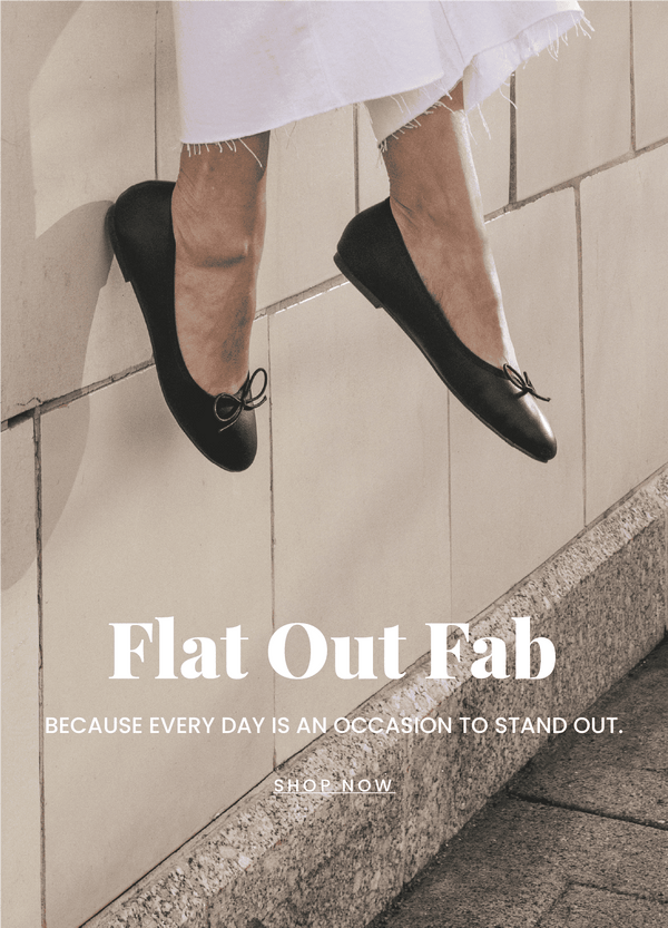 "Flat Out Fabulous" text in front of a background with a while building. A models legs are in view wearing a pair of classic black flats. "Shop Now" call to action links to the collection